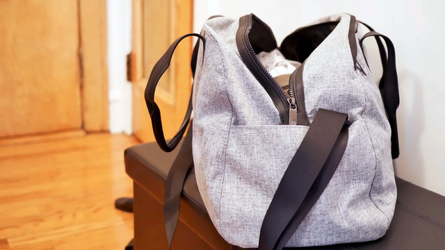 grey duffel gym bag for sport and fitness, an unbranded open bag full of clothes on the table with room background and copy space.