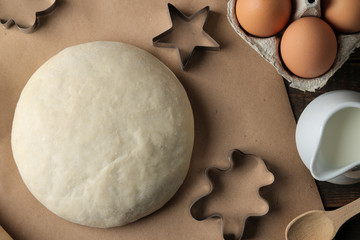 Dough and baking ingredients, biscuit forms and baking tools on a brown wooden table. view from above