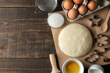 Dough and baking ingredients, biscuit forms and baking tools on a brown wooden table. top view with space for text