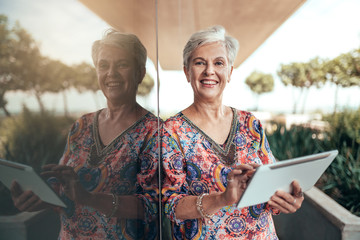 Portrait of a beautiful grey haired middle aged smiling woman working with tablet looking into the...