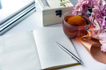 open Notepad with a clean sheet of paper, a mug of black tea, silver pen , jewelry box, hydrangea...