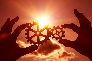 gears in the hands of a man on the background of the evening sky. the mechanism of the interaction,