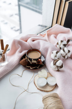 Cup of coffee with milk, candy, heart of rope, candles, cotton twig, knitted sweater, krini on the windowsill