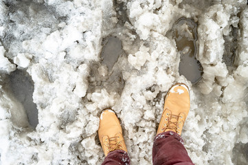 yellow boots and slush on a snowy road as an obstacle to the passage of pedestrians, printed...
