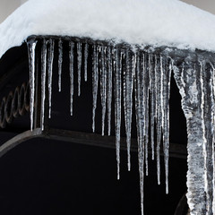 Icicles spike of ice hanging from the snowy roof. Winter subfreezing weather or spring snowbreak concept