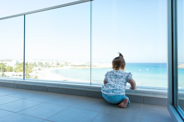 Toddler happy girl looking out at Cyprus, Mediterranean Sea from a glass balcony