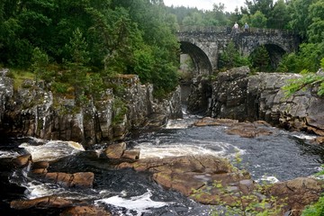 Garve, Scotland, UK: Two men walking on the Victorian-era Little Garve Bridge over Black Water, a river in the Scottish Highlands.