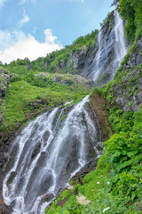 Fototapeta na wymiar High waterfall falls from the green mountain
