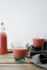 Strawberry banana smoothie in glasses and bottle. Rustic wooden table, white background