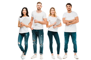Fototapeta na wymiar happy young people in white t-shirts and jeans holding laptops and smiling at camera isolated on white