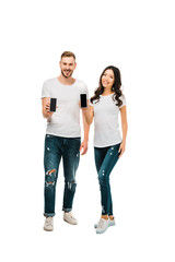 Obraz premium happy young couple holding smartphones with blank screens and smiling at camera isolated on white
