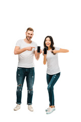 happy young couple pointing at smartphones with blank screens isolated on white