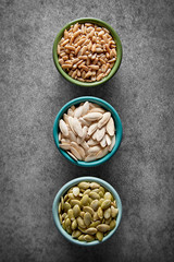 Pumpkin (peeled, salted, roasted) and sunflower seeds in a bowls on a dark background viewed from above. Top view