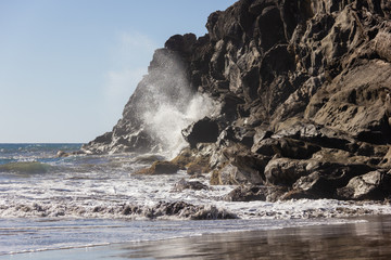 Sea water crashing on rock cliff on sunny day at the beach. Violent impact of wave on shore