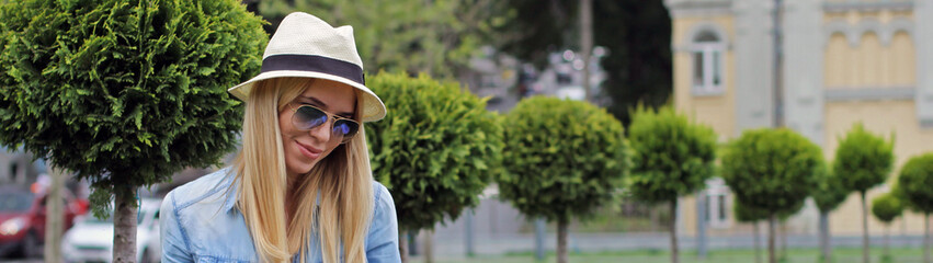 The girl the blonde in the hat beautifully smiling sitting on the summer green lawn