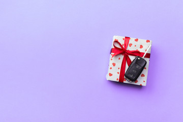 Car key on paper gift box with red ribbon bow and heart on violet table background. Holidays present top view concept