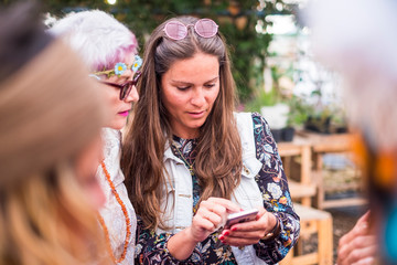Hippy fashion style trendy group of mixed ages caucasian women using technology modern phone together - beautiful females with coloured dress and clothes enjoying internet device