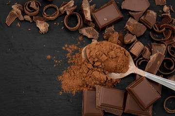 Broken chocolate pieces and cocoa powder on a dark background. Top view with copyspace