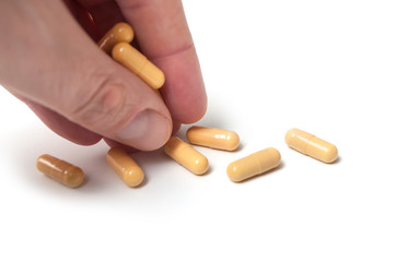 closeup of man taking yellow drug capsules with fingers on white background