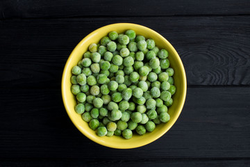 Frozen peas  in the  yellow bowl  on the black wooden background.Top view.Copy space.Healthy food ingredient.