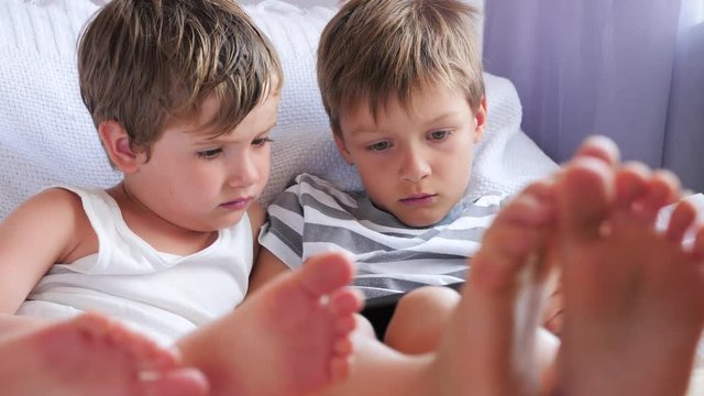 Social communication disorder. Two boys holding smartphone, tablet sitting on chair, focus on childrens feet.