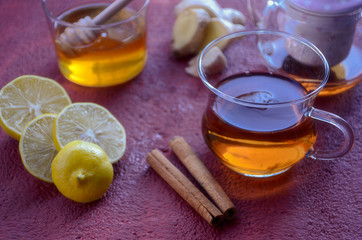 Healthy winter drink concept. Antiviral useful drink ginger tea with lemon, honey and slices of ginger on wooden red and orange background.