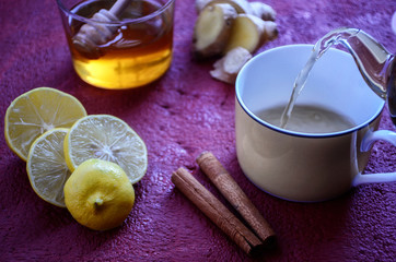 Healthy winter drink concept. Antiviral useful drink ginger tea with lemon, honey and slices of ginger on wooden red and orange background.