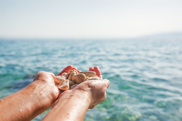 Female hands on the background of sea or ocean are holding sea stones.