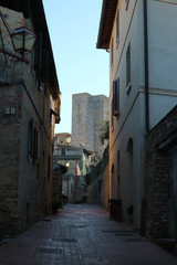 Fototapeta na wymiar Medieval narrow street in old town San Gimignano with the famous towers at the background, Tuscany, Italy