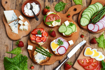Set of healthy whole wheat bread sandwiches with fuits, vegetables, cheese and leafy green herbs on picnic wooden table. Ciabatta sandwich bar. Top view. Lunch time snacks concept. Vegetarian food