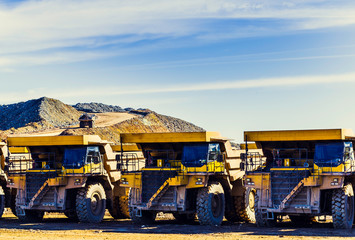 Big yellow dumper trucks placed in a row in the mine with dumper trucks laden with ore on the...