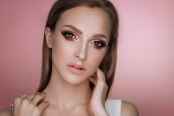  portrait of a beautiful elegant brunette girl with makeup and haircut in the studio on a pink background