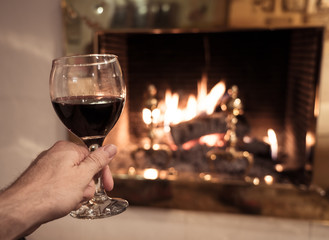 Close up of happy man drinking wine relaxing by fire place at home in winter holidays vacation