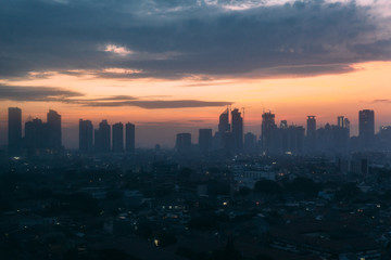 Jakarta Cityscape with high rise, skyscrapers and red tile hip roof local buildings with fog and early morning sky at dawn in background.