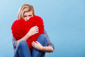 Sad woman holding red pillow in heart shape