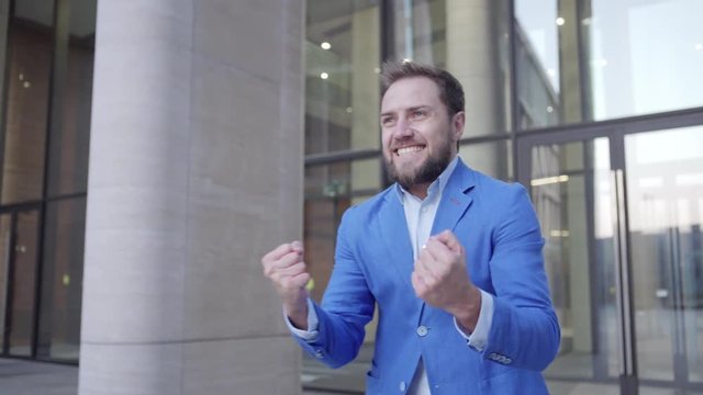 Satisfied manager leaving business center and celebrating with yes gesture after successful business meeting