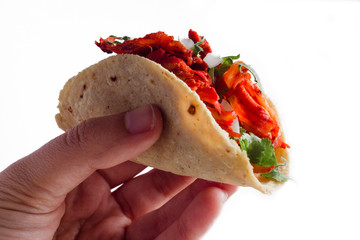 Close-up of a hand holding authentic mexican taco al pastor on a white background