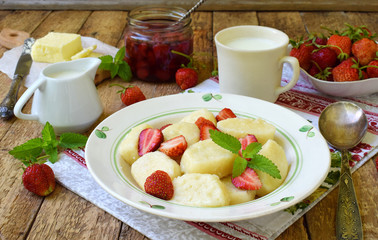 Sweet lazy pierogi. Ukrainian dumplings with sour cream, butter and strawberry on wooden background. Summer berry breakfast. Italian gnocchi. Copy space