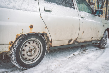 The bottom of the doors and the bottom of the white car in winter is covered with a caustic iron...