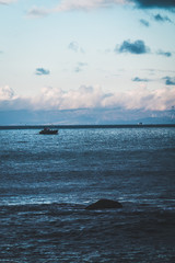 Fototapeta premium Fishing boat in the sea, under beautiful clouds, Spain's coast in the background (Strait of Gibraltar)