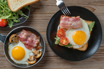 Top view of fried eggs on black plate and pan with fork, mushrooms and rukkola