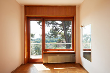 Empty room interior with large window and wooden floor in country house, sunlight