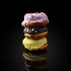 A stack of donuts with icing and chocolate powder, reflected in the mirror. On a black background, isolate, copy space.