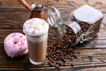 A donut with pink icing and chocolate powder and a cappuccino glass with high foam and decoration....