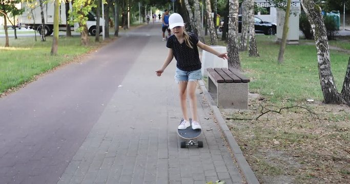 A sweet girl in a cap skates on a skateboard in the park.