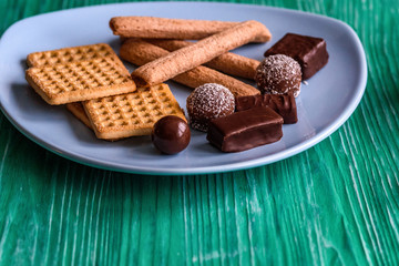 Shortbread cookies and chocolates on a btruzy plate, standing on a green wooden background.
