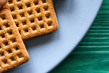 Shortbread cookies and chocolates on a btruzy plate, standing on a green wooden background.