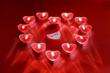 Wedding solitaire ring in heart shaped red box with heart shaped candle on red background. Valentine's day concept.