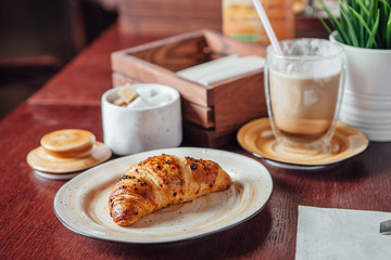 Croissant dusted with chocolate chips and a glass cup with cocoa on a dark wood table in the bar