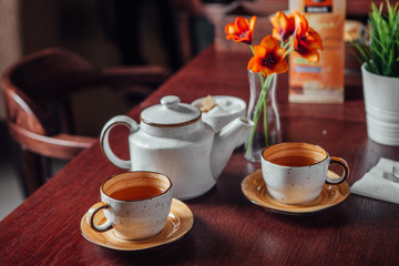 Two cups of tea with a kettle stand on a dark wood table in a cafe